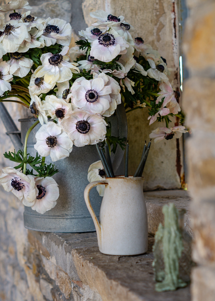 white anemones on a windowsill of a rustic stone house